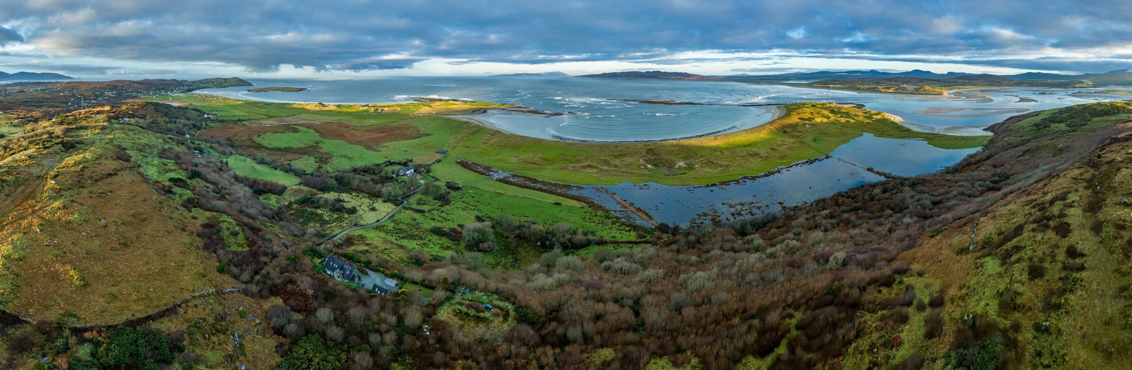 A coastal landscape with a large body of water, green fields, and a small house.