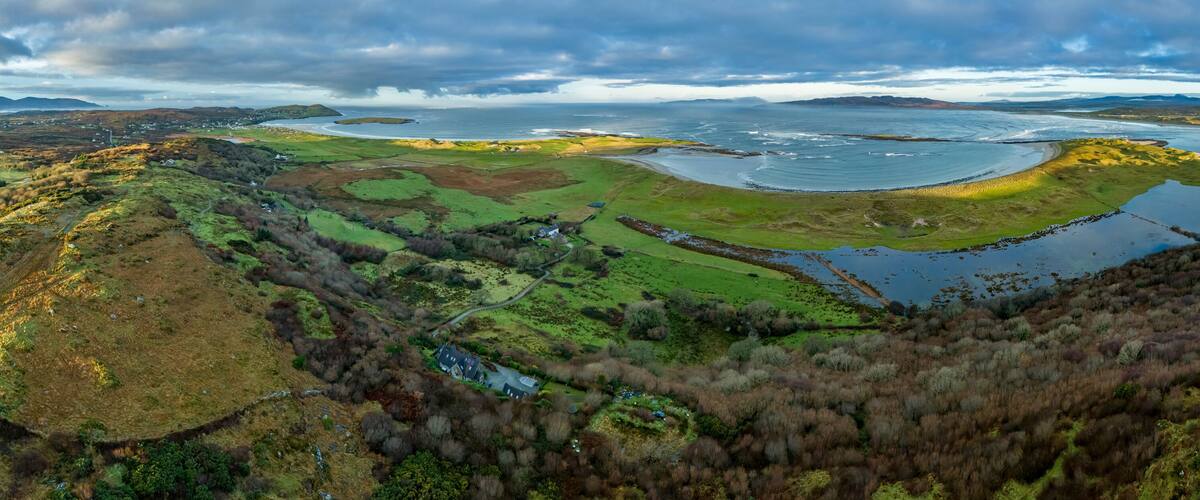 A coastal landscape with a large body of water, green fields, and a small house.
