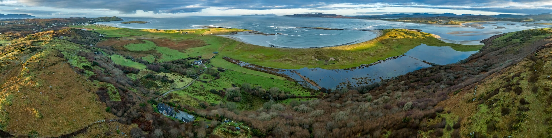 A coastal landscape with a large body of water, green fields, and a small house.