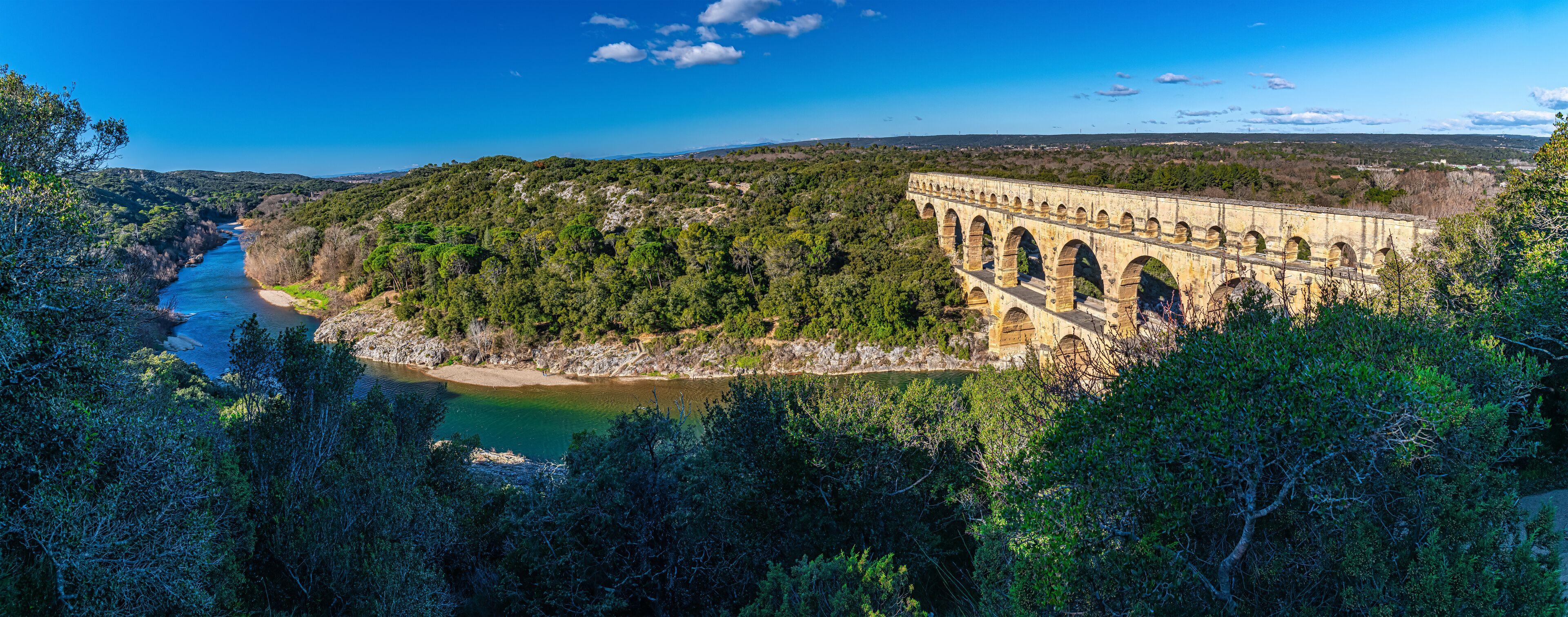 A large dam with multiple arches, surrounded by dense forest and a river flowing through a valley.