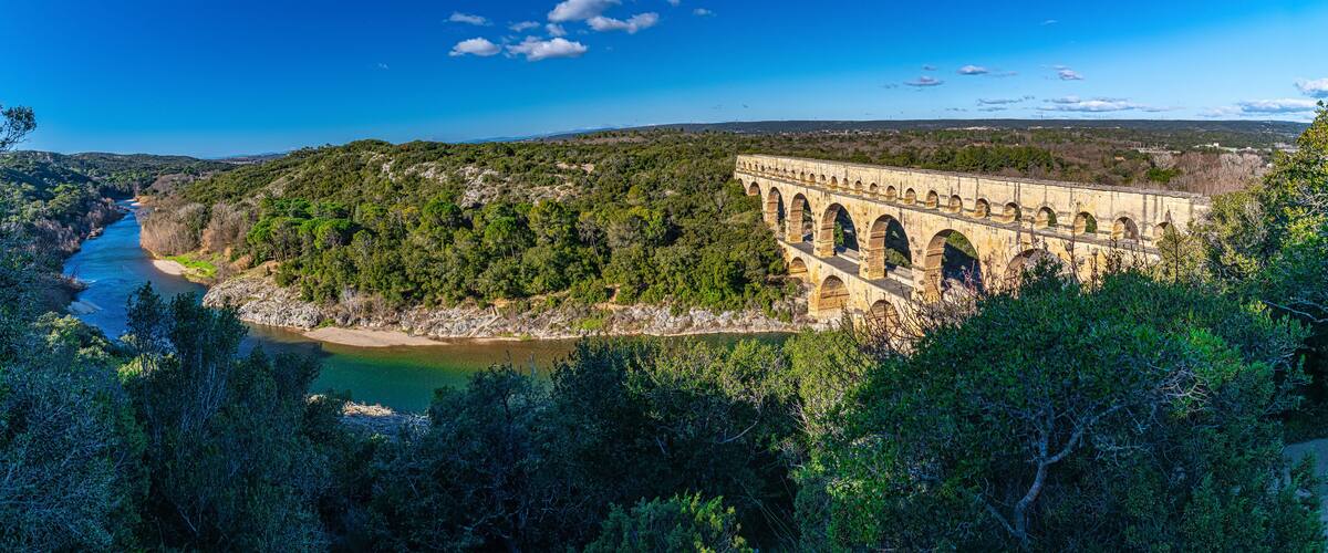 A large dam with multiple arches, surrounded by dense forest and a river flowing through a valley.