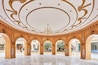 An ornate hall with a large chandelier, marble floor, and golden ceiling decorations.