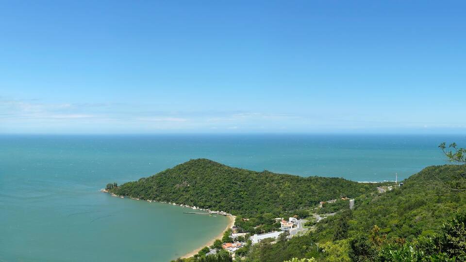 A coastal landscape with a beach, lush green hills, and a clear blue sky.