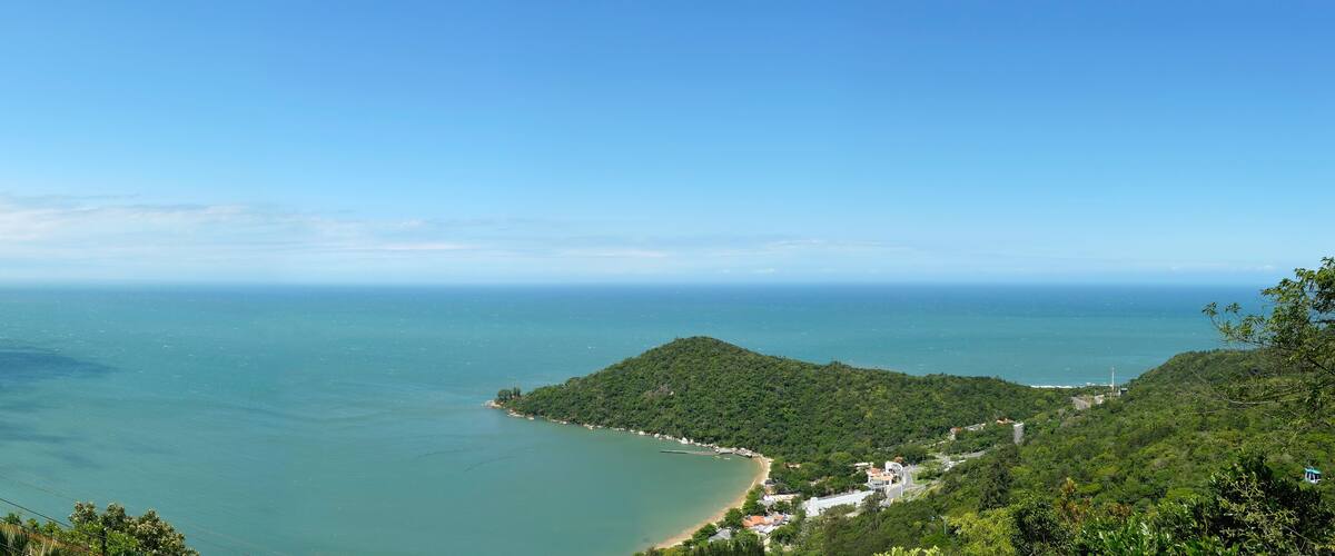 A coastal landscape with a beach, lush green hills, and a clear blue sky.