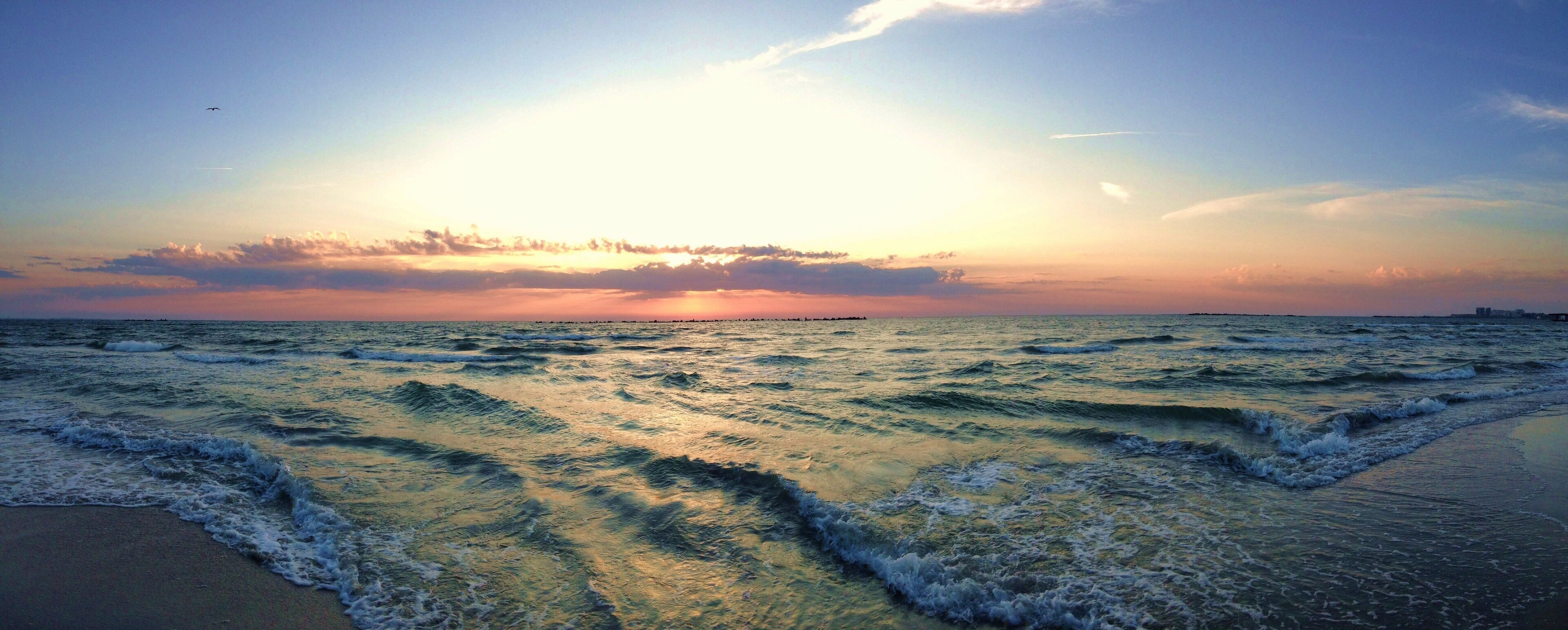 A sunset over the ocean with waves crashing onto the shore.