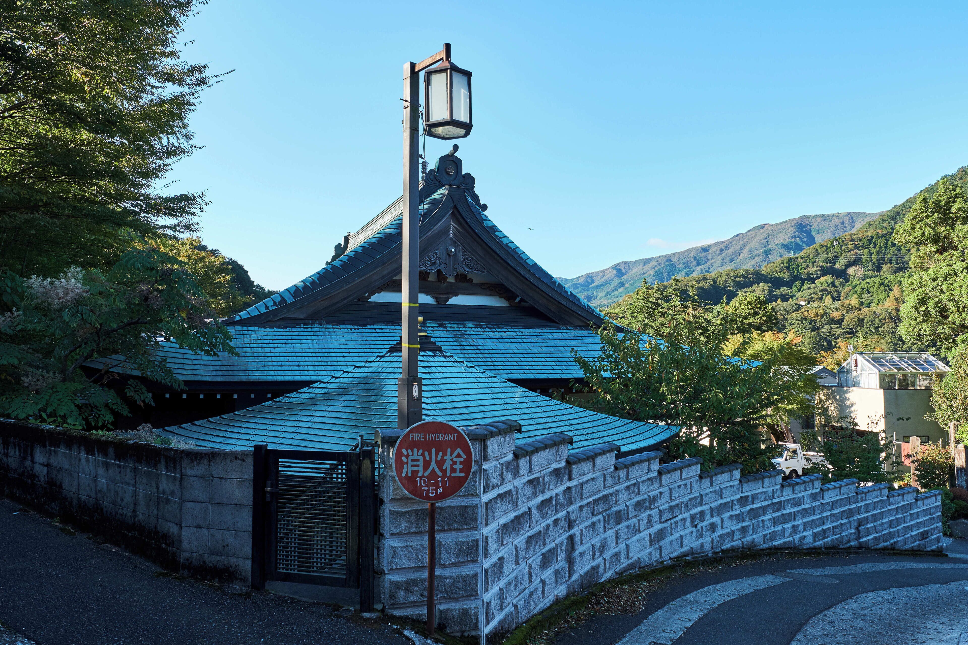A traditional Japanese building with a blue roof, a stone wall, and a fire hydrant sign.