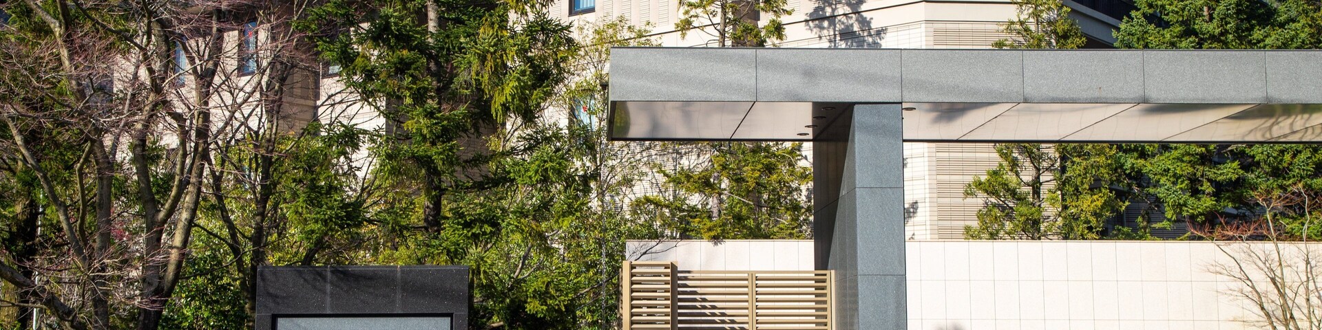 Um edifício moderno com uma placa na frente, rodeado por árvores e um cenário montanhoso.
