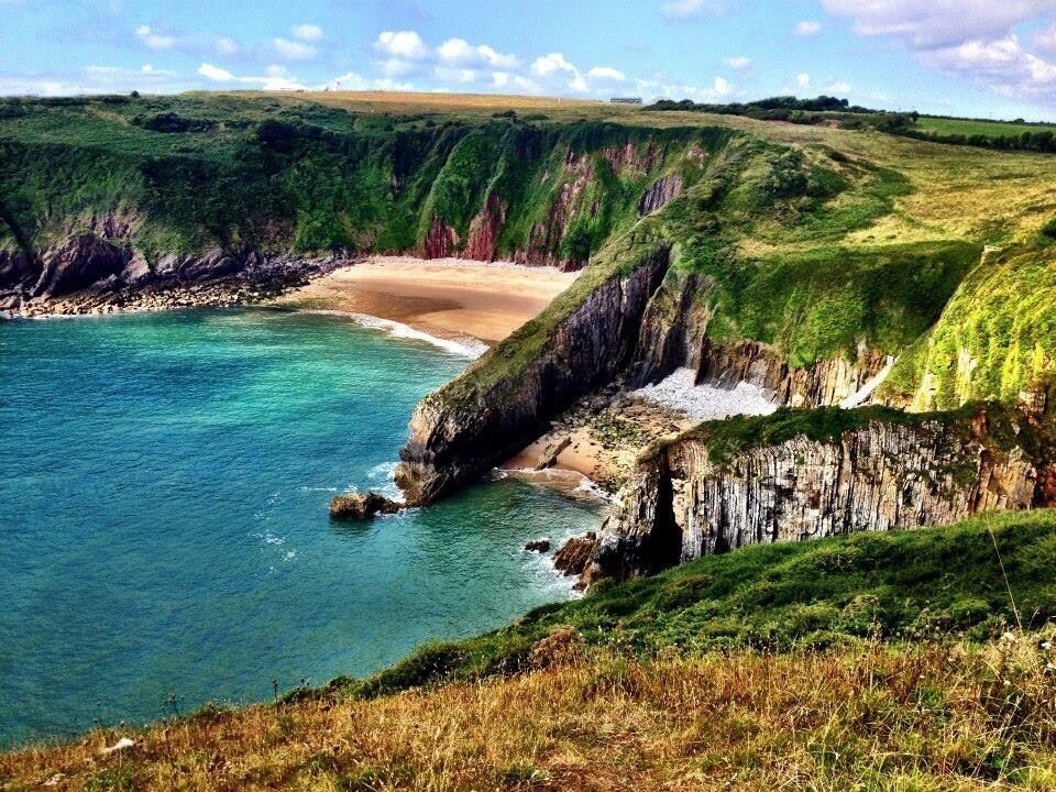 A coastal landscape with cliffs, a beach, and clear blue waters.