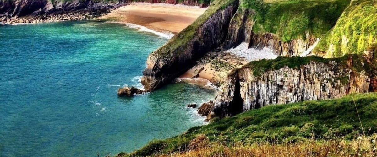 A coastal landscape with cliffs, a beach, and clear blue waters.
