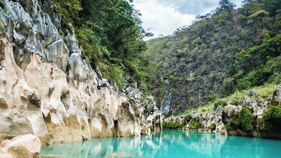 A turquoise river with rocky cliffs and lush greenery.