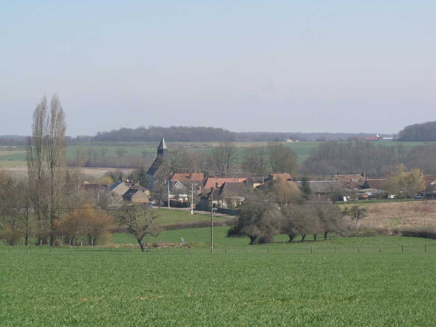 Un paysage rural avec une église, des maisons et des champs à perte de vue.