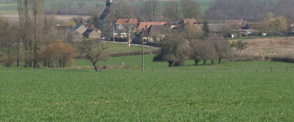 A rural landscape with a church, houses, and open fields.