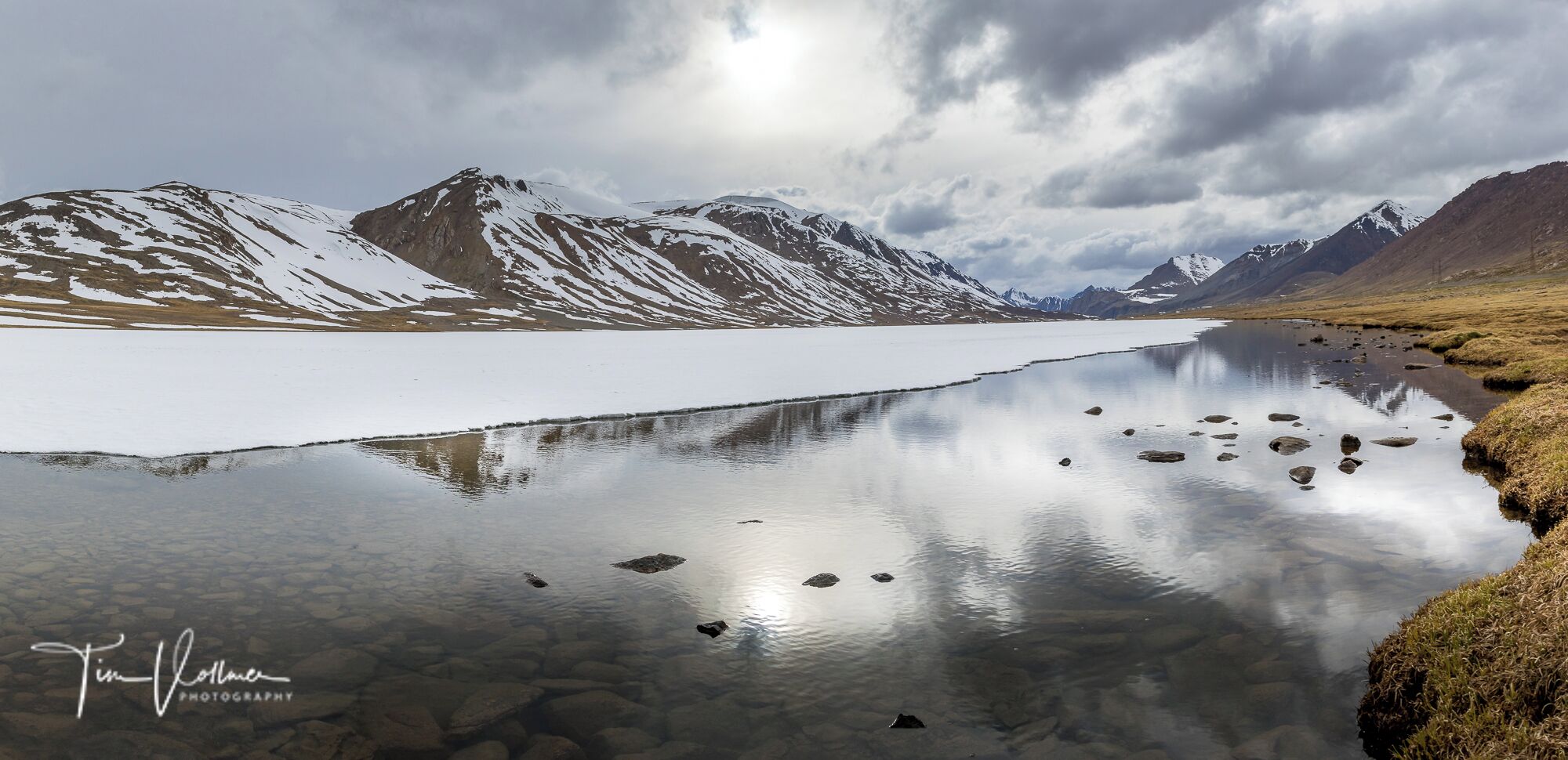 Un lago tranquilo con montañas nevadas al fondo y un cielo nublado.