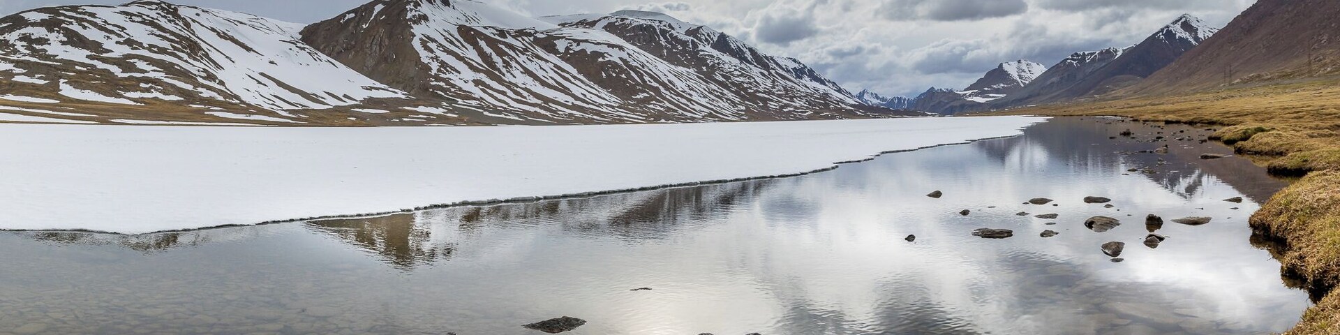 Un lago tranquilo con montañas nevadas al fondo y un cielo nublado.