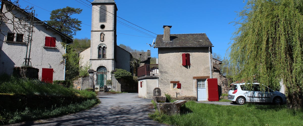 A quaint village street with a church, a white car, and red shutters on buildings.