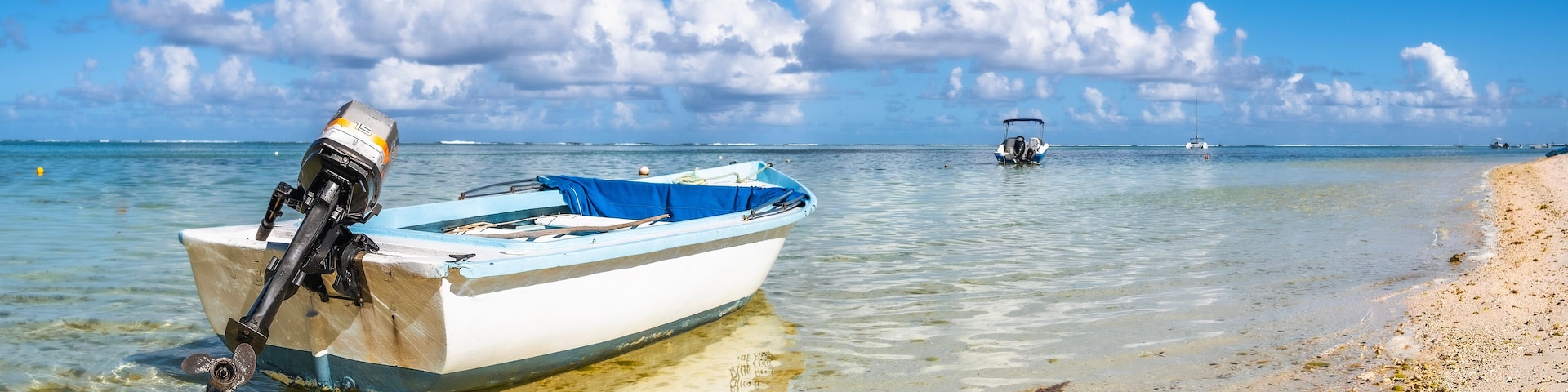 A boat on a beach with clear water and a partly cloudy sky.