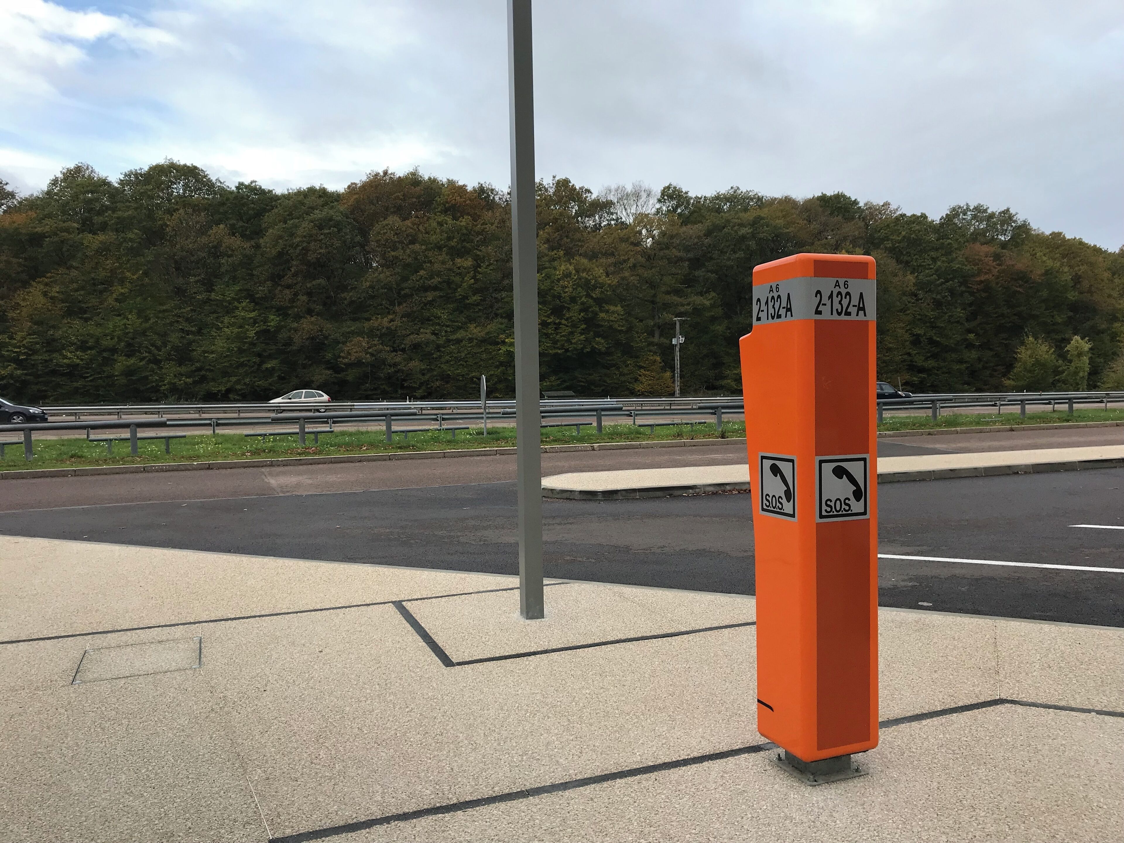 An orange roadside sign with emergency contact symbols and route numbers.