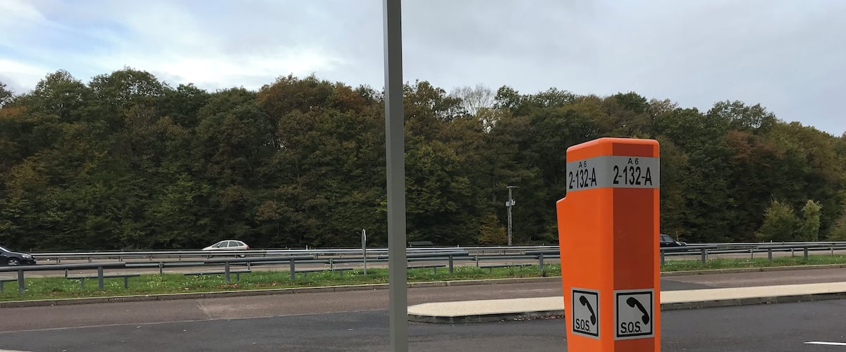 An orange roadside sign with emergency contact symbols and route numbers.