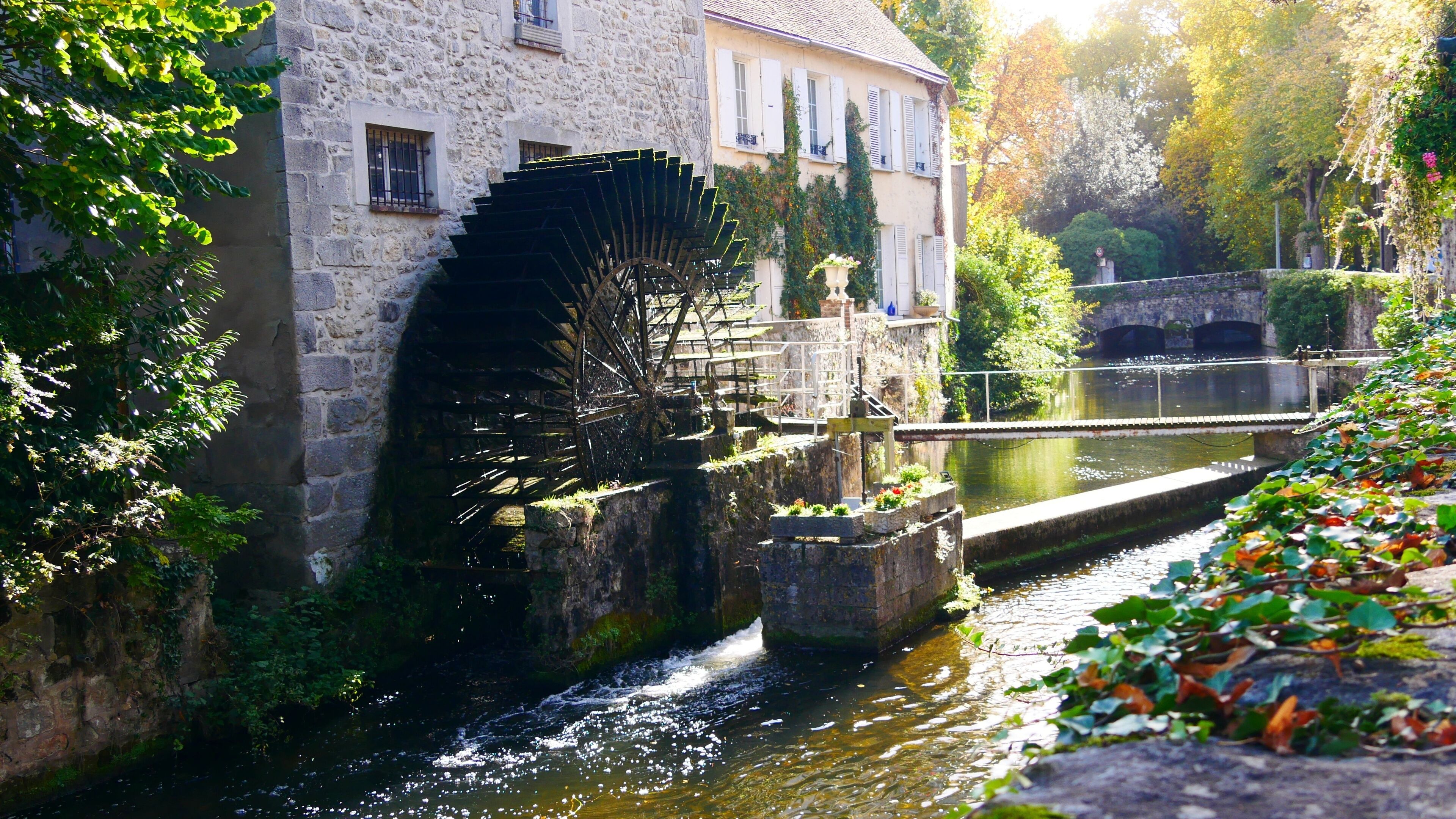 A historic stone building with a large water wheel, a canal, and lush greenery.