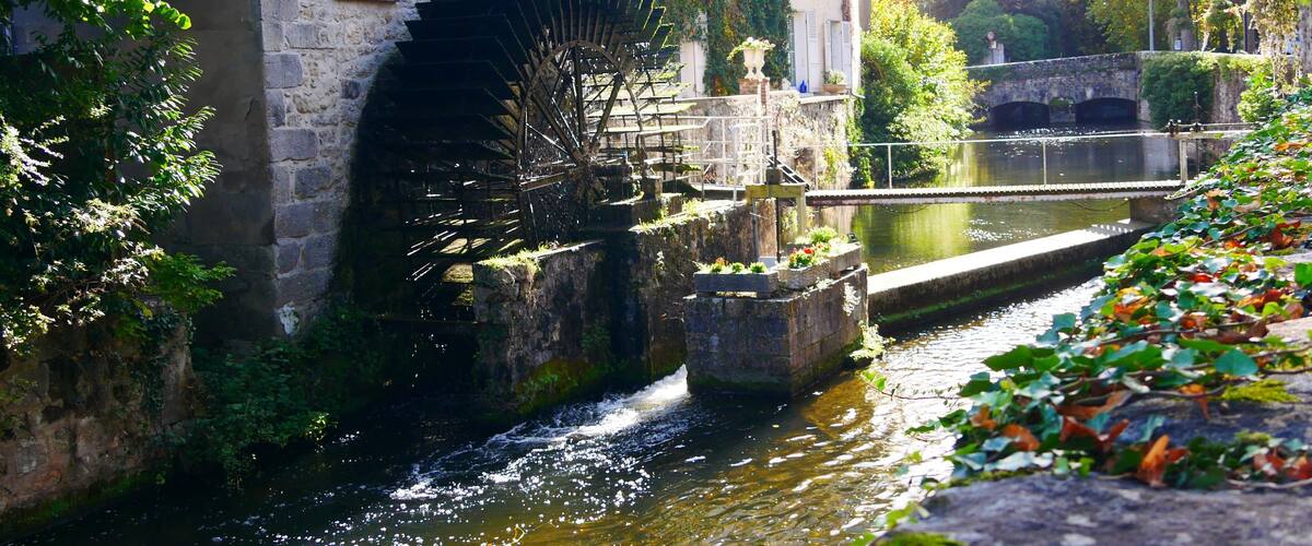 A historic stone building with a large water wheel, a canal, and lush greenery.