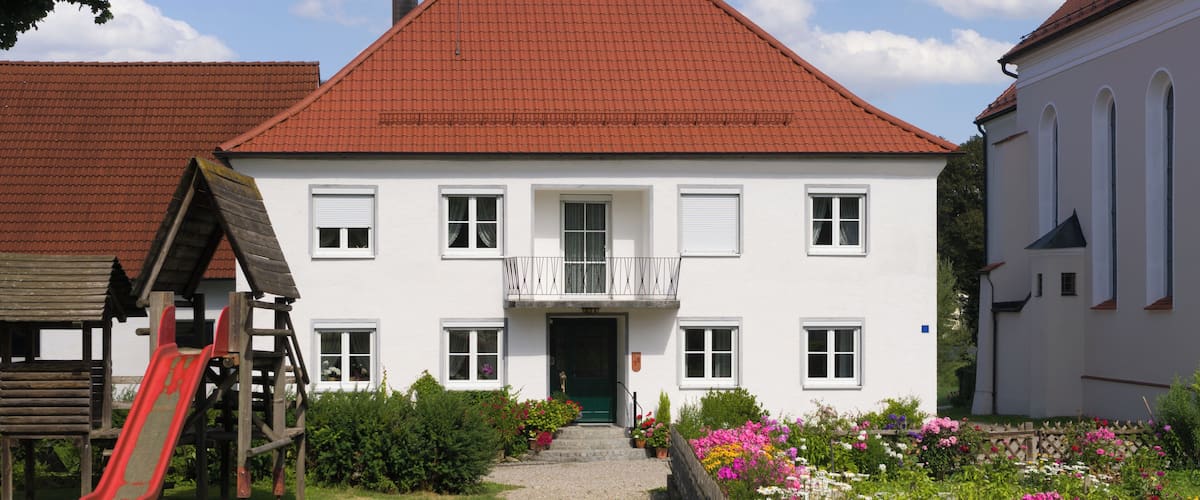 A white building with a red roof, a wooden play structure, and a garden with colorful flowers.