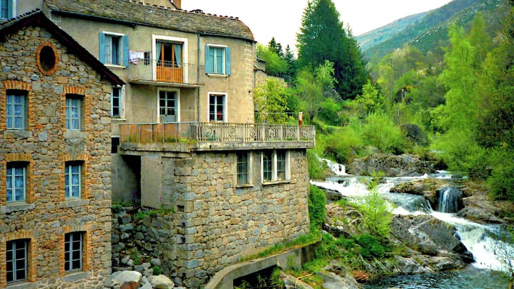Un bâtiment en pierre doté d’un balcon donnant sur une rivière et une cascade.