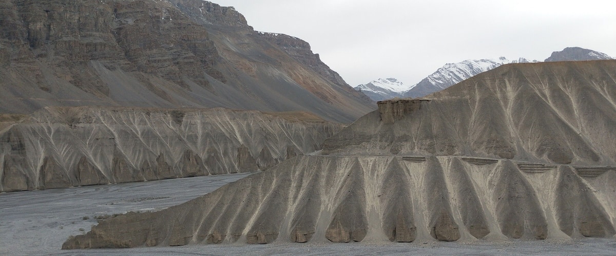 A dry, rocky landscape with layered sedimentary rock formations and a riverbed.