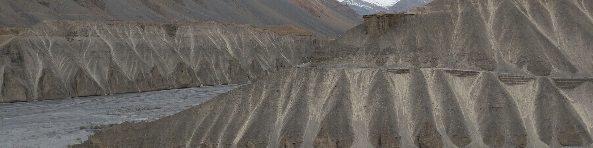 A dry, rocky landscape with layered sedimentary rock formations and a riverbed.