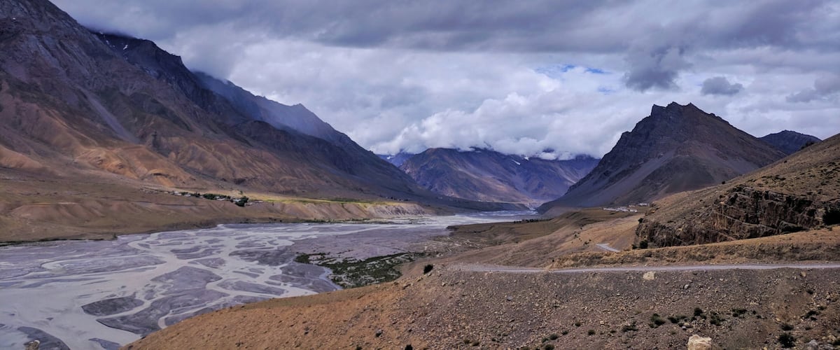 Un río serpentea por un paisaje montañoso, con terreno accidentado y cumbres lejanas.