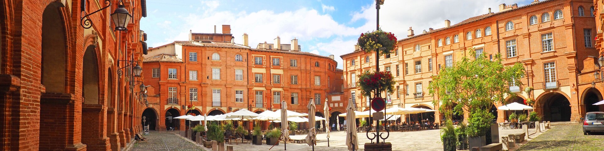 A cobblestone courtyard with red brick buildings, outdoor seating, and hanging flower baskets.