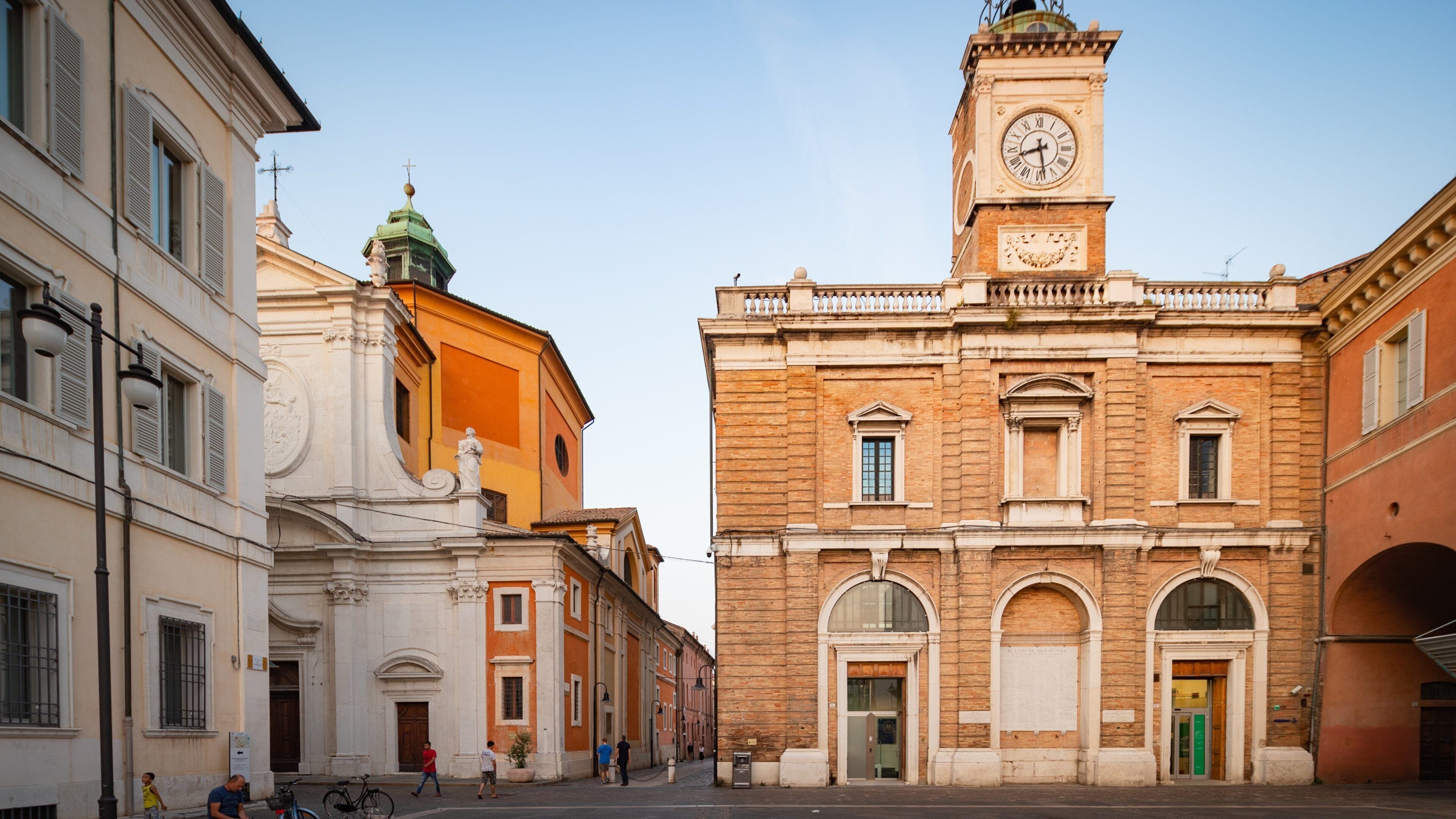 A street with historic buildings, a clock tower, and a statue.