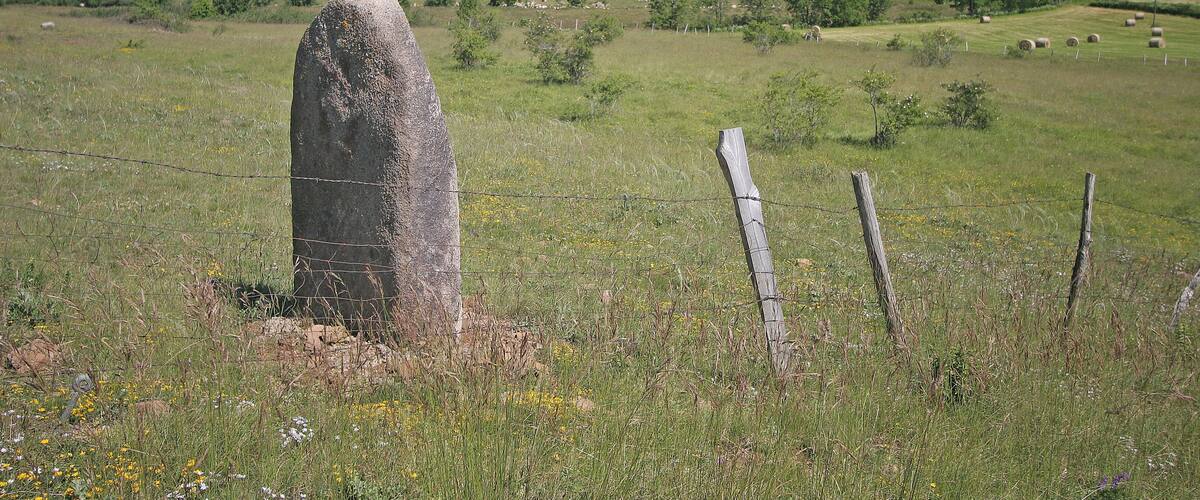 A stone monument in a grassy field with a fence and rolling hills in the background.