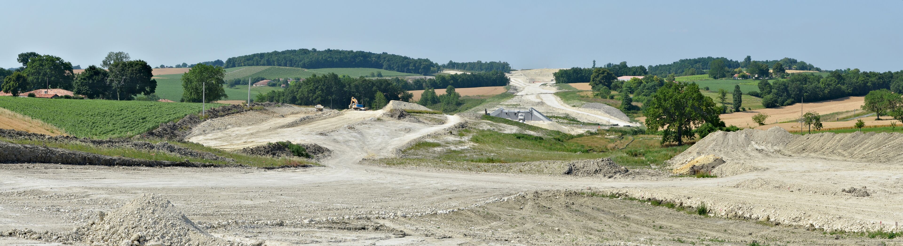 A construction site with a dirt road, excavators, and a large pile of gravel.