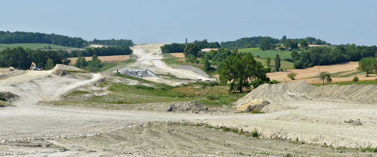 A construction site with a dirt road, excavators, and a large pile of gravel.