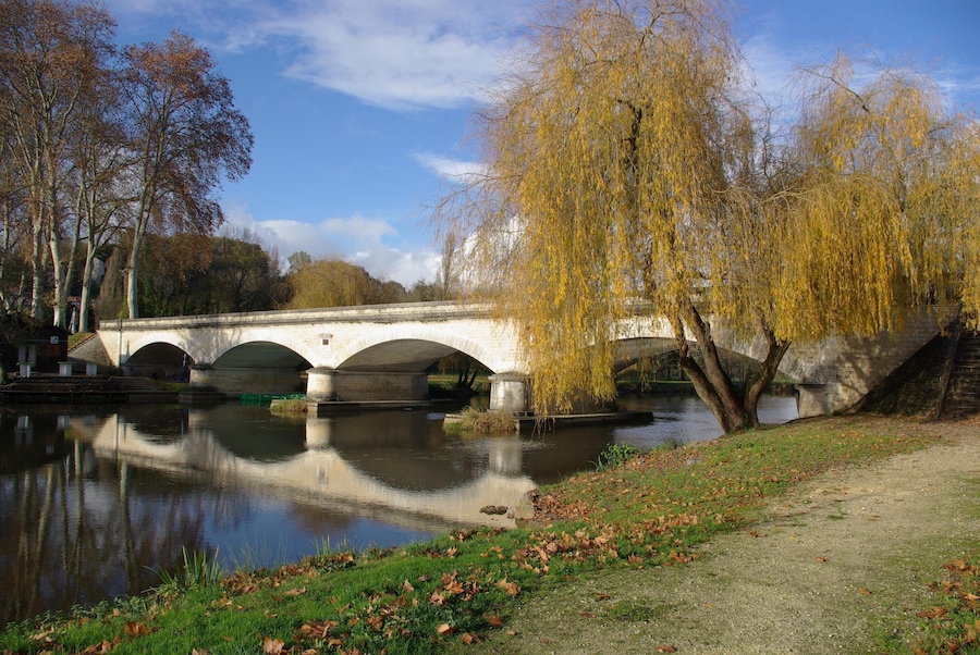 Een stenen brug over een rustige rivier, omgeven door bomen en een grasrijke oever.