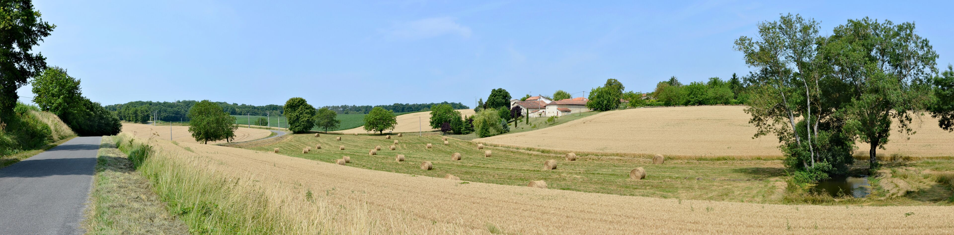 A rural landscape with rolling hills, hay bales, a road, and a few houses.