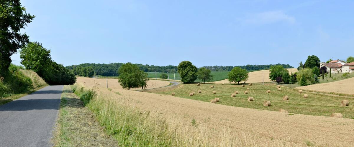 A rural landscape with rolling hills, hay bales, a road, and a few houses.