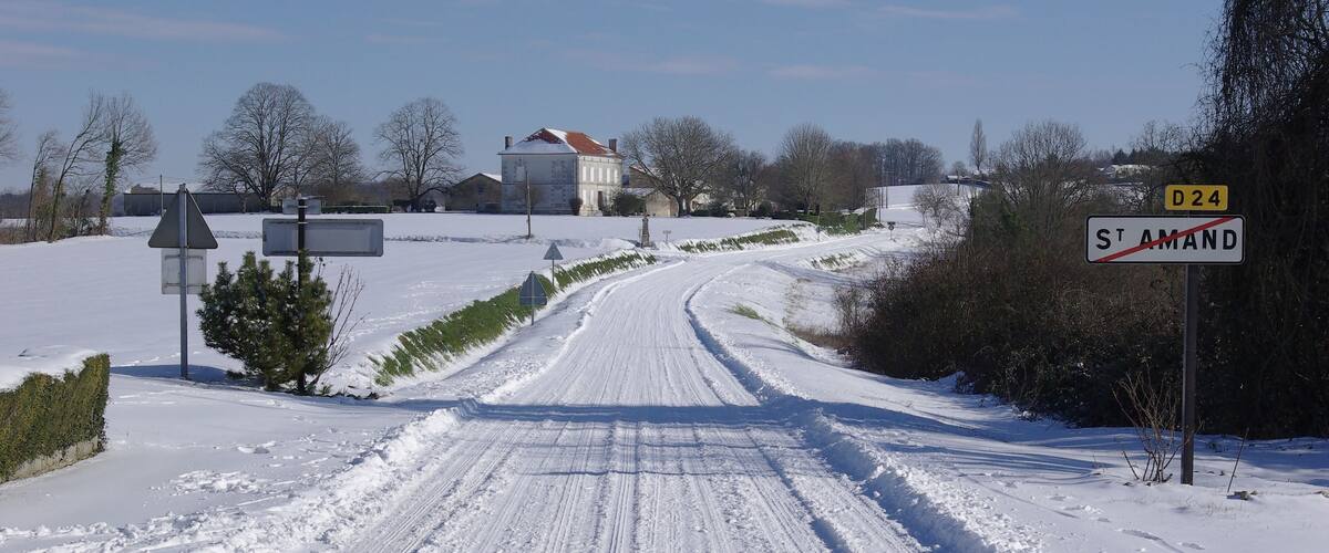 Une route de campagne enneigée, avec un panneau indiquant la direction de la D24 et de Saint-Amand.