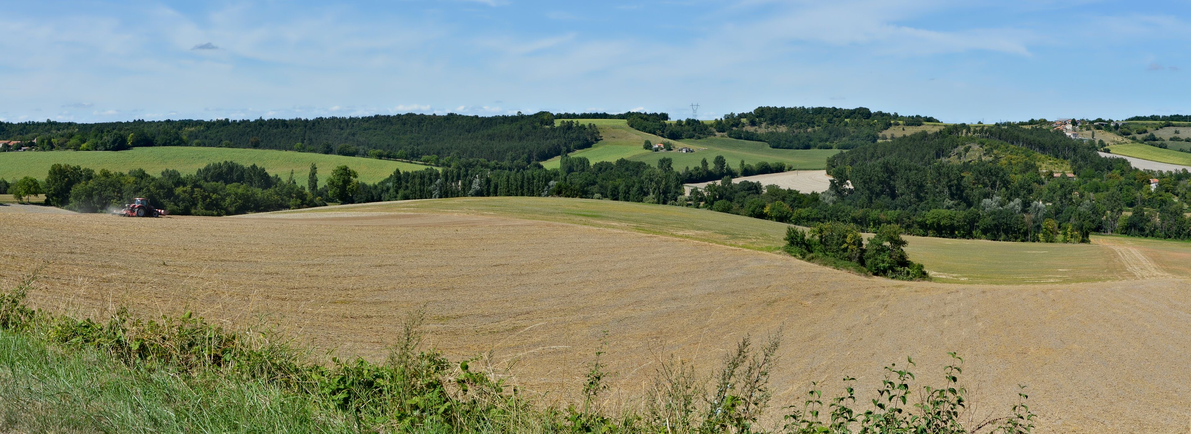 A rural landscape with rolling hills, a tractor in a field, and scattered houses.