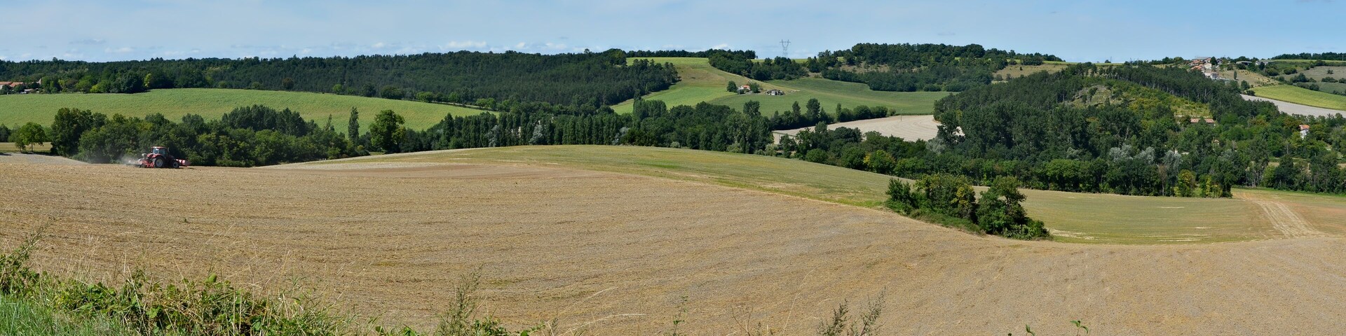 A rural landscape with rolling hills, a tractor in a field, and scattered houses.