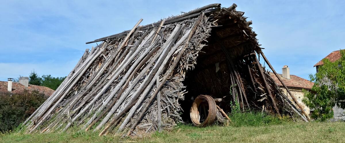 A rustic wooden structure with a thatched roof, surrounded by grass and trees.