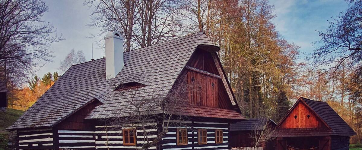 A traditional log cabin with a sloped roof and wooden walls, surrounded by a gravel path and a wooden fence.