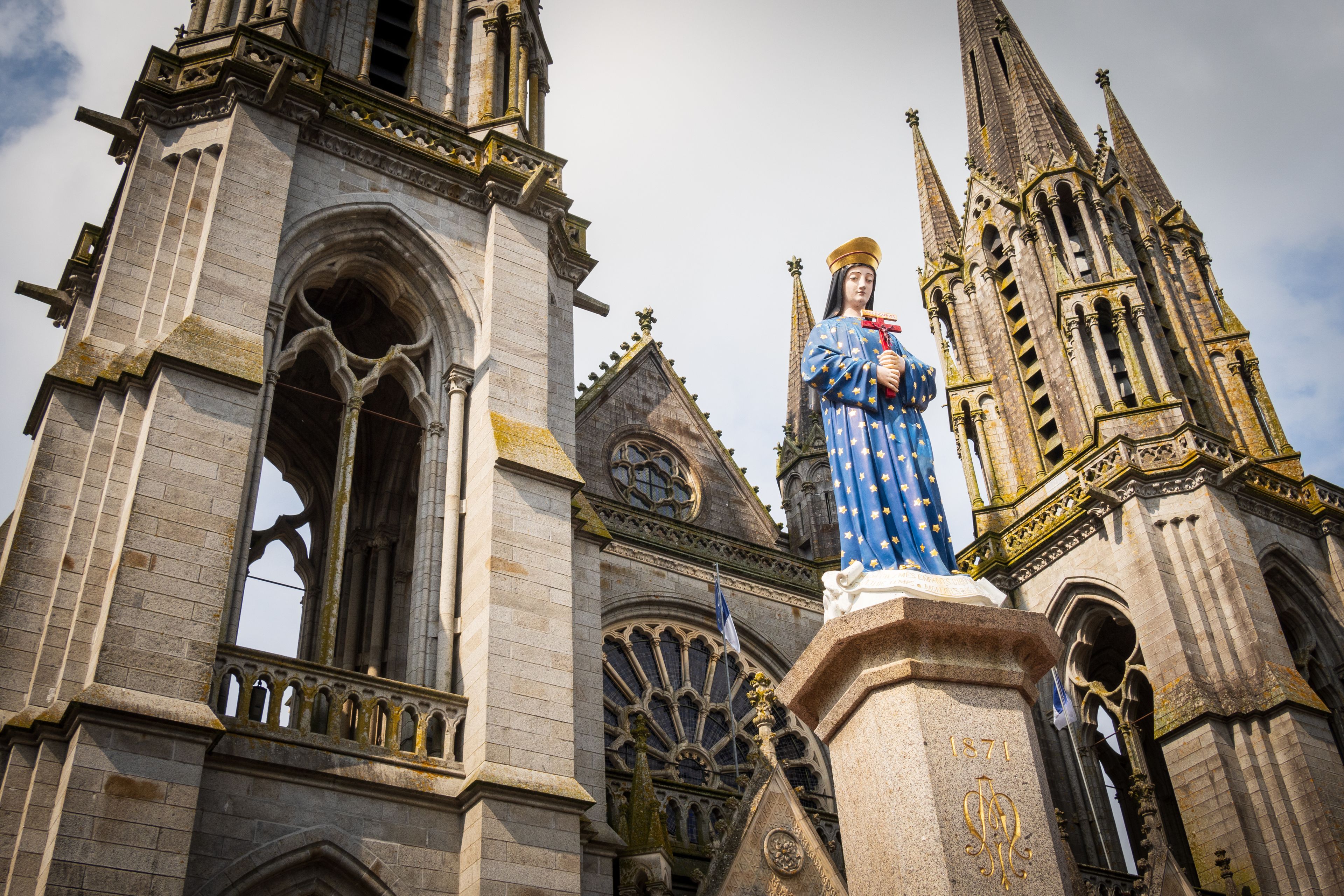 A Gothic church with a statue of a saint, intricate stonework, and a tall spire.