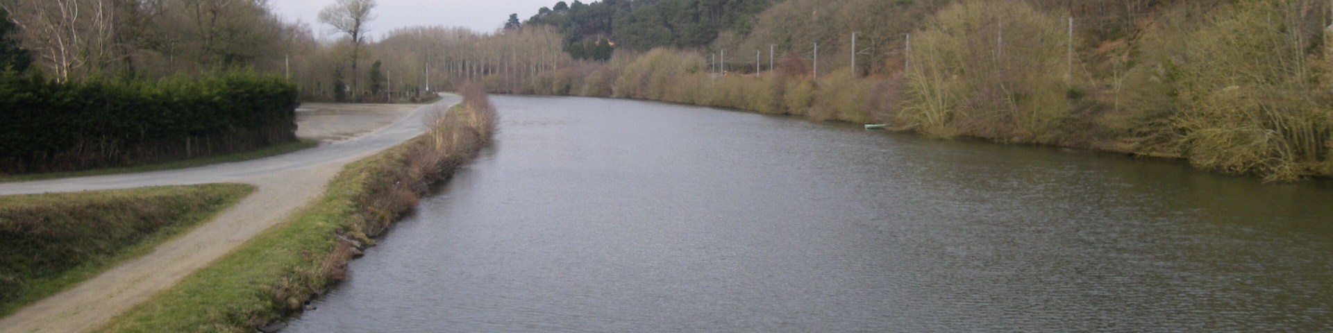 A river with a grassy bank and trees on the left, a road curving alongside, and a forested hill on the right.
