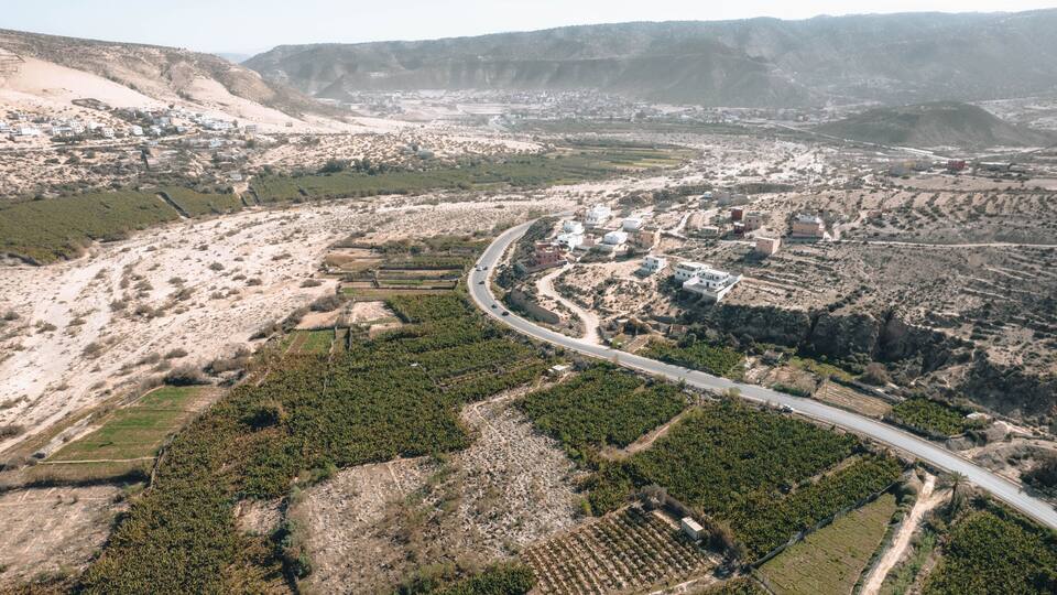 An aerial view of a hilly landscape with a winding road, scattered buildings, and agricultural fields.