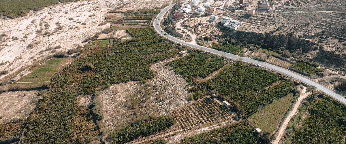An aerial view of a hilly landscape with a winding road, scattered buildings, and agricultural fields.