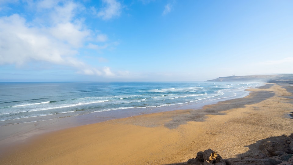 A sandy beach with gentle waves and a clear blue sky.