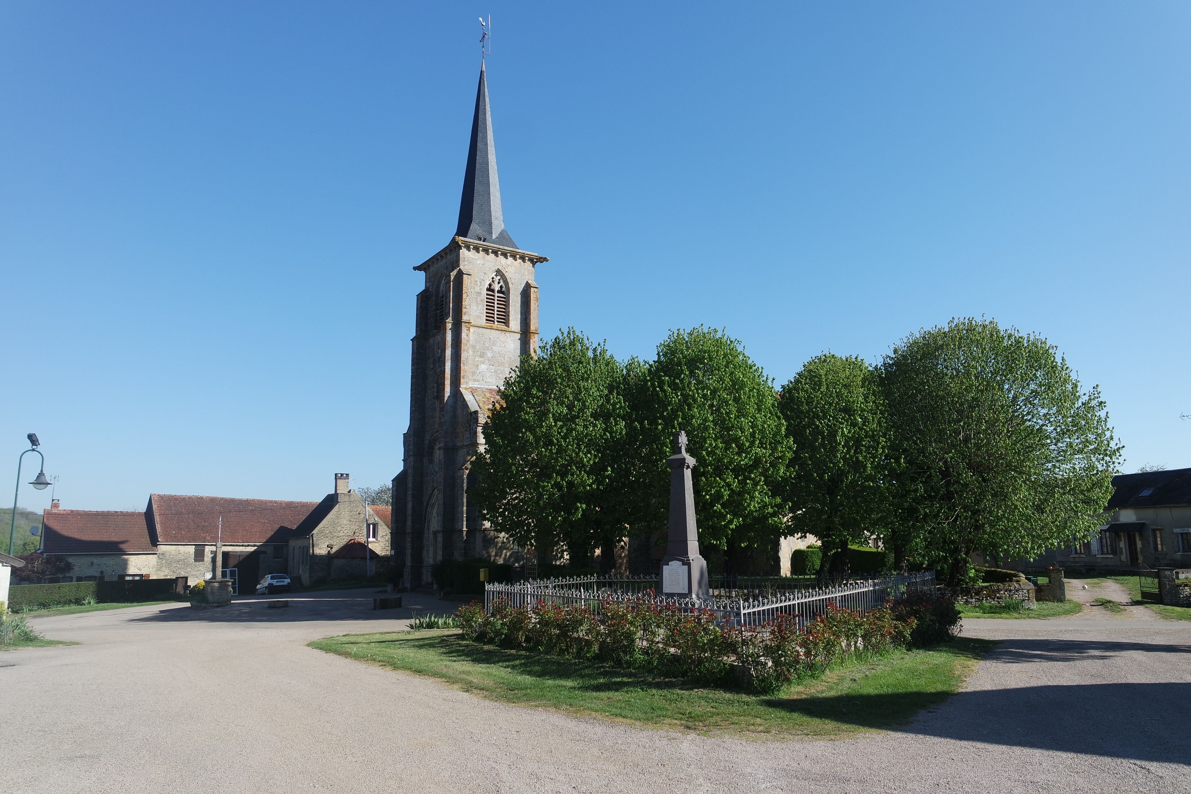 A church with a tall steeple, a memorial cross, and a paved road leading to it.