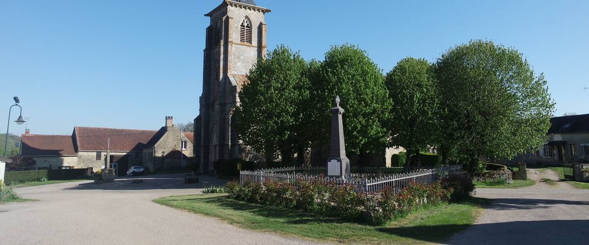 A church with a tall steeple, a memorial cross, and a paved road leading to it.