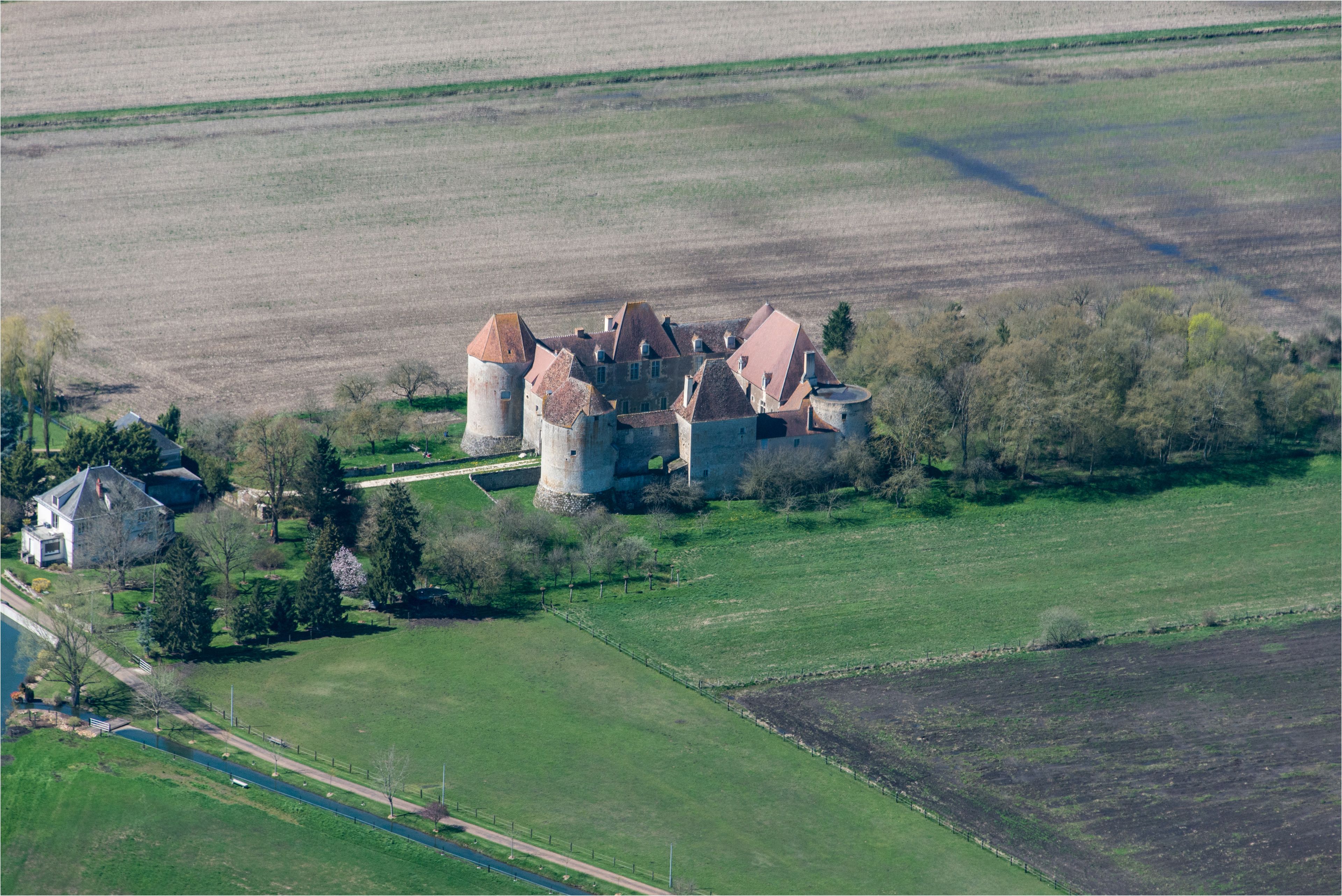 Une vue aérienne d’un château doté de nombreuses tours, entouré de champs et d’un petit village.